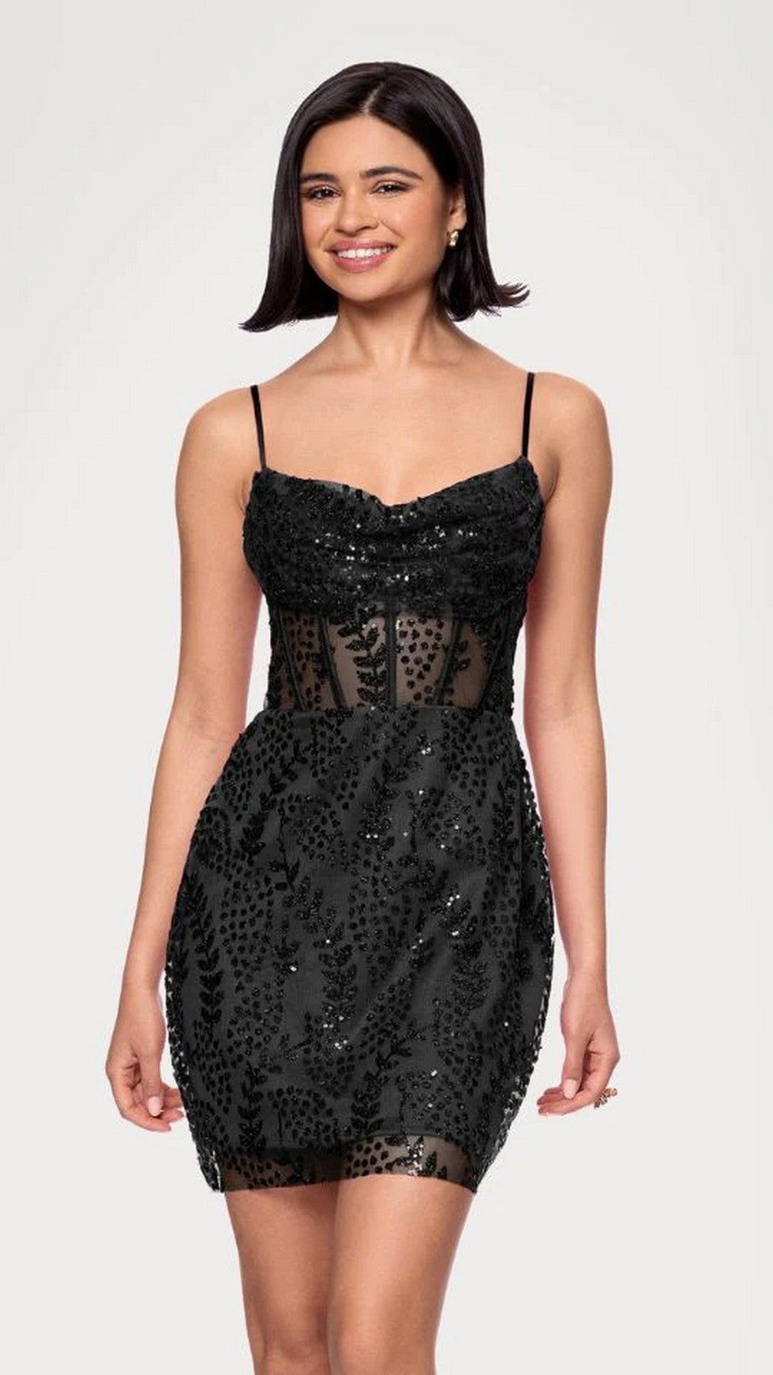 Woman in a black Short Prom Dress (Blondie Nites 5570BN) with thin straps and sheer paneling, standing and smiling against a plain light background.